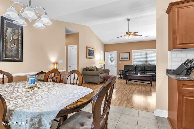 dining space with light tile patterned floors, ceiling fan with notable chandelier, baseboards, and vaulted ceiling