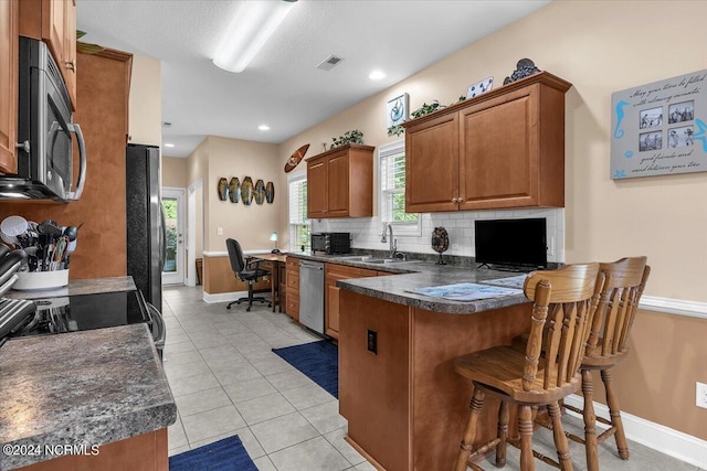 kitchen with a sink, dark countertops, backsplash, stainless steel appliances, and a peninsula