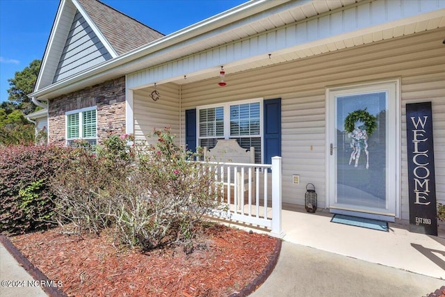 property entrance featuring a porch, stone siding, and a shingled roof