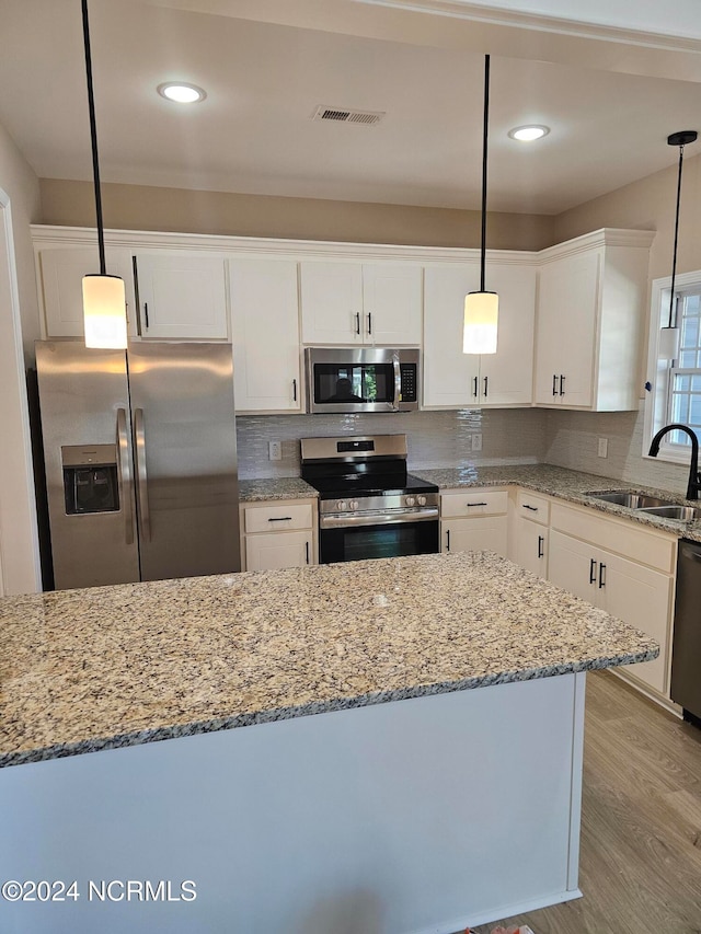 kitchen with pendant lighting, white cabinetry, sink, light hardwood / wood-style floors, and stainless steel appliances