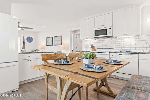 kitchen with white cabinetry, backsplash, dark stone counters, light hardwood / wood-style floors, and white appliances