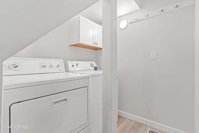 laundry area with separate washer and dryer, light hardwood / wood-style floors, and cabinets