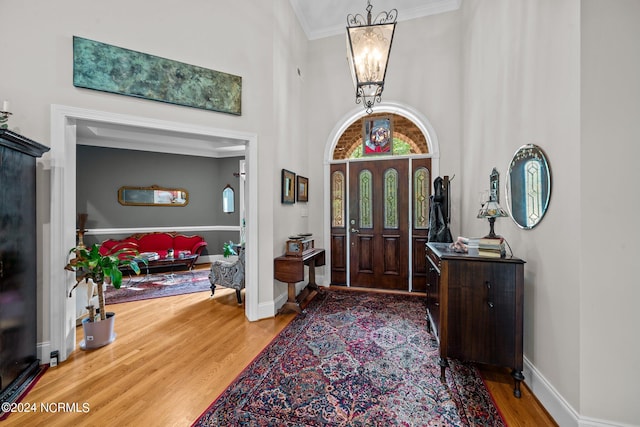 foyer entrance featuring wood-type flooring, crown molding, a notable chandelier, and a towering ceiling