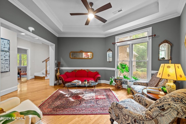 living room with a raised ceiling, ceiling fan, ornamental molding, and hardwood / wood-style floors