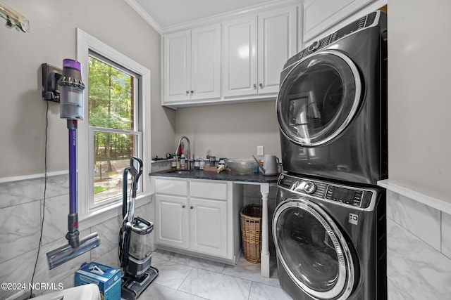 clothes washing area with a wealth of natural light, crown molding, cabinets, and stacked washer / dryer