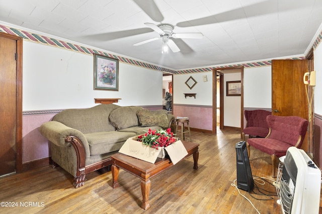 living room featuring a wainscoted wall, light wood finished floors, heating unit, and a ceiling fan