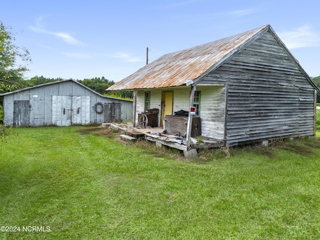 back of property with an outbuilding, metal roof, an outdoor structure, and a lawn