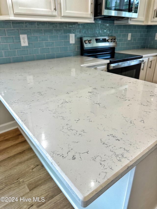 kitchen featuring light stone countertops, appliances with stainless steel finishes, backsplash, and hardwood / wood-style floors