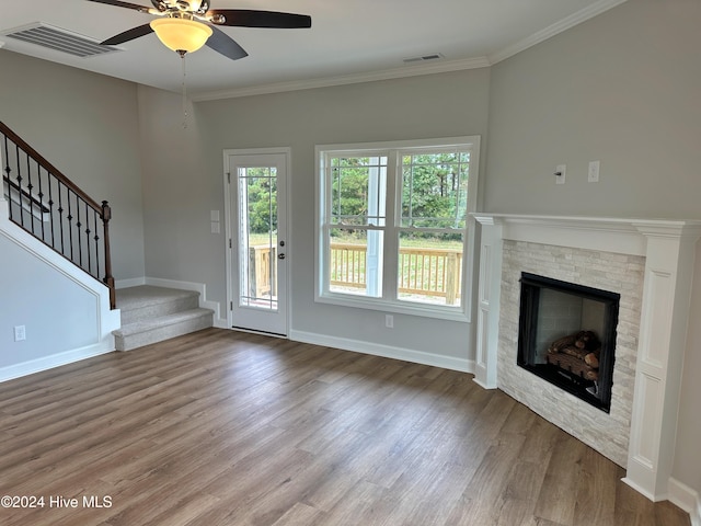 unfurnished living room with a stone fireplace, ceiling fan, crown molding, and hardwood / wood-style flooring