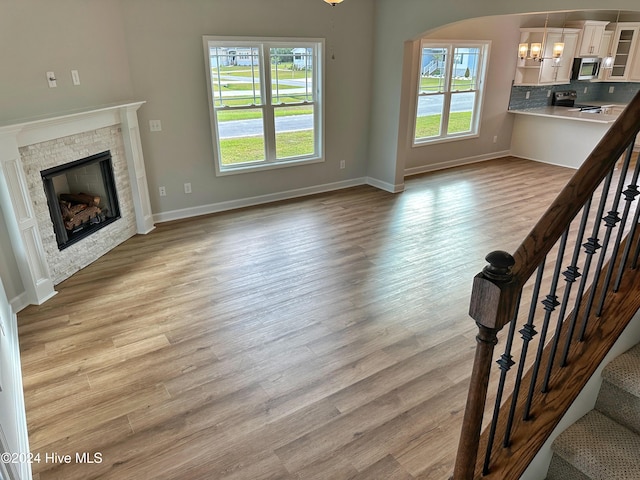 unfurnished living room with a fireplace, a healthy amount of sunlight, a notable chandelier, and light hardwood / wood-style floors