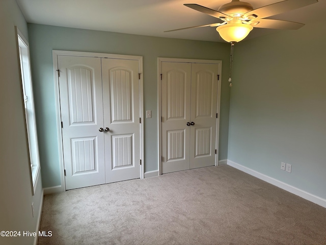 unfurnished bedroom featuring ceiling fan, light colored carpet, and two closets