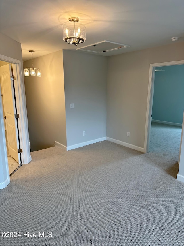 empty room with light colored carpet and an inviting chandelier