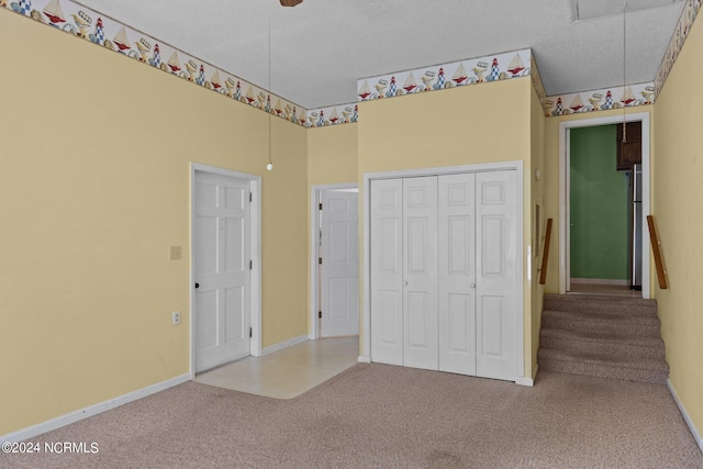 unfurnished bedroom with a textured ceiling, carpet floors, stainless steel refrigerator, and a closet