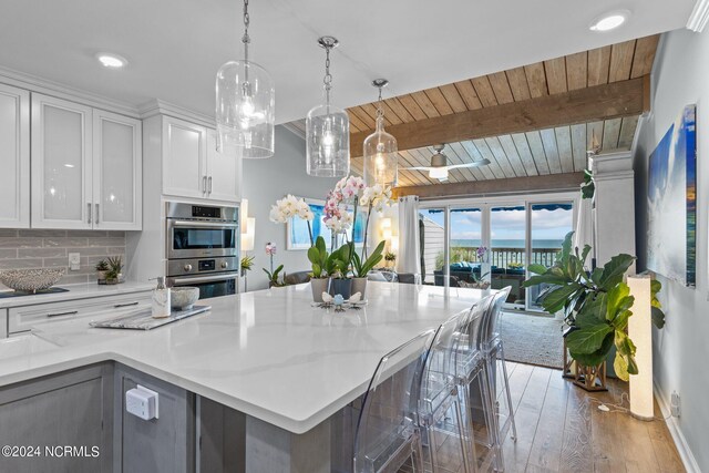 kitchen featuring beamed ceiling, hanging light fixtures, ceiling fan, light stone countertops, and white cabinets