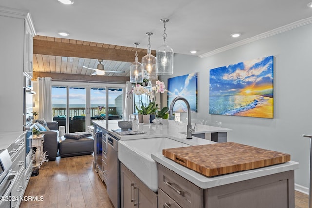 kitchen featuring lofted ceiling with beams, light wood-type flooring, decorative light fixtures, appliances with stainless steel finishes, and a kitchen island with sink