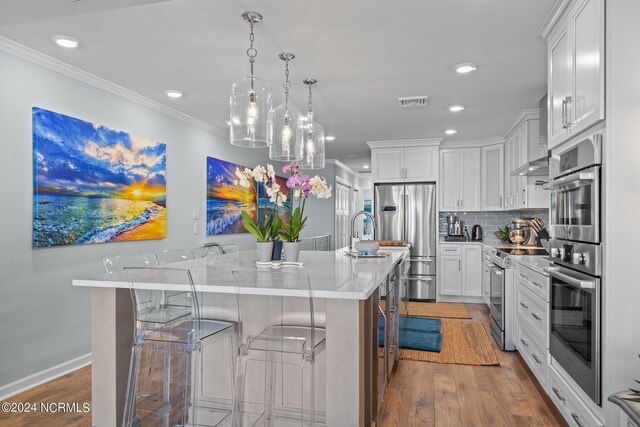 kitchen featuring white cabinets, light hardwood / wood-style flooring, decorative light fixtures, stainless steel appliances, and a breakfast bar area