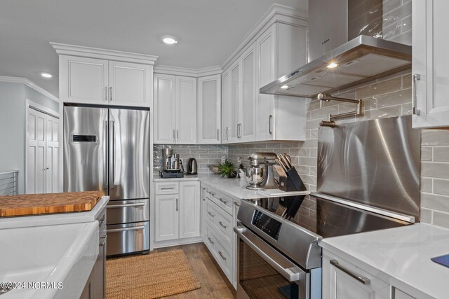 kitchen with crown molding, decorative backsplash, appliances with stainless steel finishes, white cabinets, and wall chimney range hood