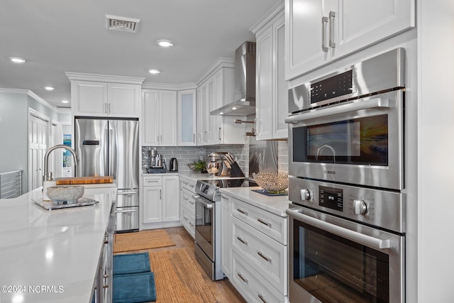 kitchen featuring white cabinets, light stone counters, stainless steel appliances, wall chimney exhaust hood, and ornamental molding