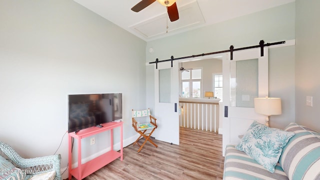 living area with attic access, a barn door, a ceiling fan, baseboards, and wood finished floors
