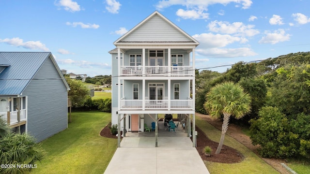 raised beach house featuring a front yard, a carport, concrete driveway, and a balcony