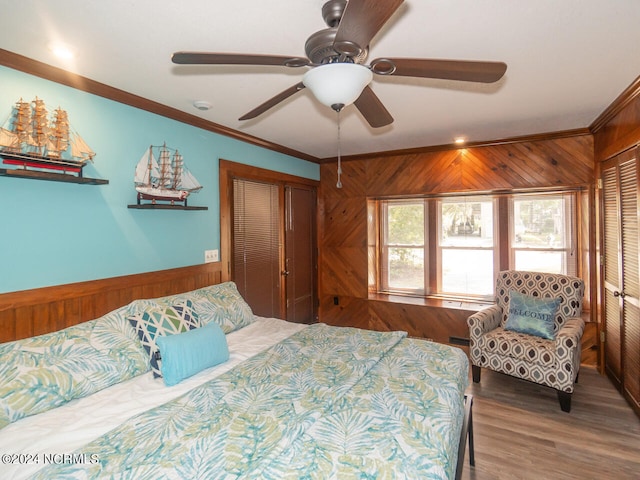 bedroom with hardwood / wood-style floors, wood walls, ceiling fan, ornamental molding, and a closet