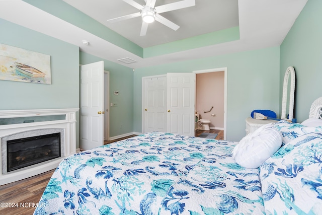 bedroom featuring ceiling fan, a raised ceiling, ensuite bath, and dark hardwood / wood-style flooring