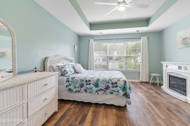 bedroom with ceiling fan, a raised ceiling, and dark wood-type flooring