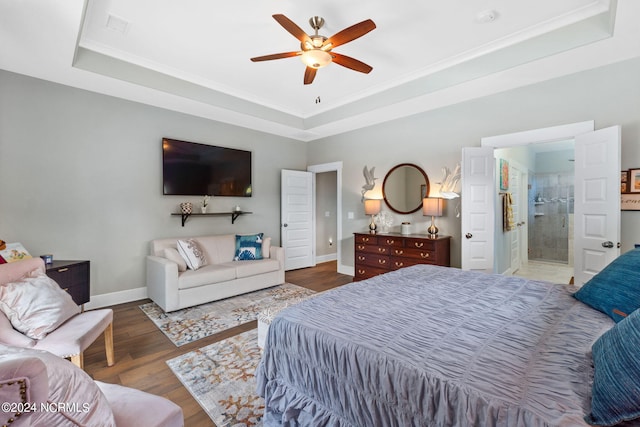 bedroom with dark wood-type flooring, ensuite bath, a raised ceiling, and ceiling fan