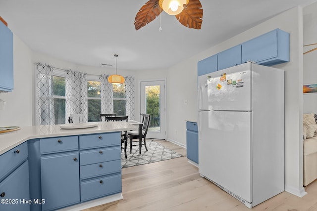 kitchen featuring blue cabinetry, white refrigerator, light hardwood / wood-style flooring, and hanging light fixtures