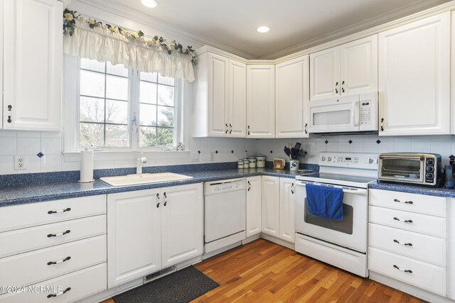 kitchen with white appliances, backsplash, light hardwood / wood-style floors, sink, and white cabinets