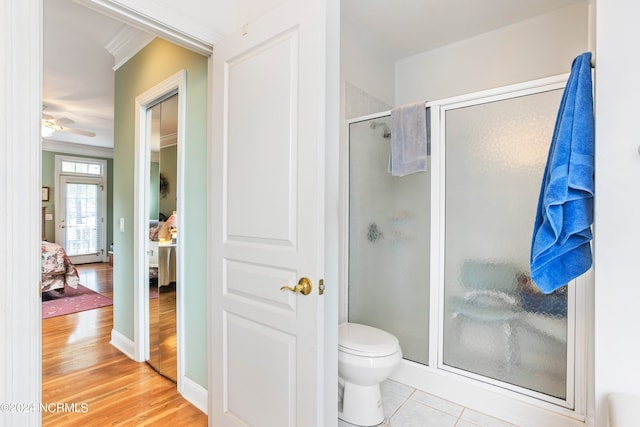 bathroom with a shower with door, hardwood / wood-style flooring, toilet, ceiling fan, and ornamental molding