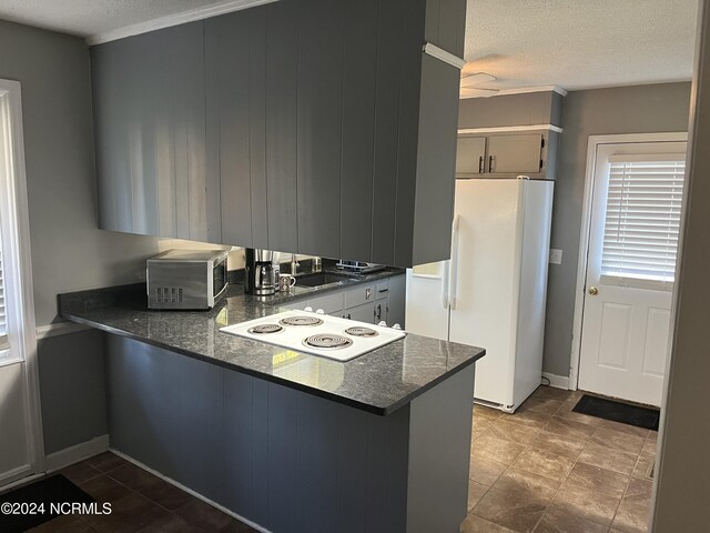 kitchen with a textured ceiling, kitchen peninsula, white appliances, and dark stone counters