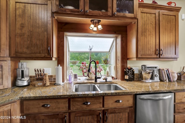 kitchen featuring dishwasher, light stone countertops, glass insert cabinets, and a sink