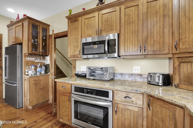 kitchen with brown cabinets, wood finished floors, stainless steel appliances, a toaster, and glass insert cabinets