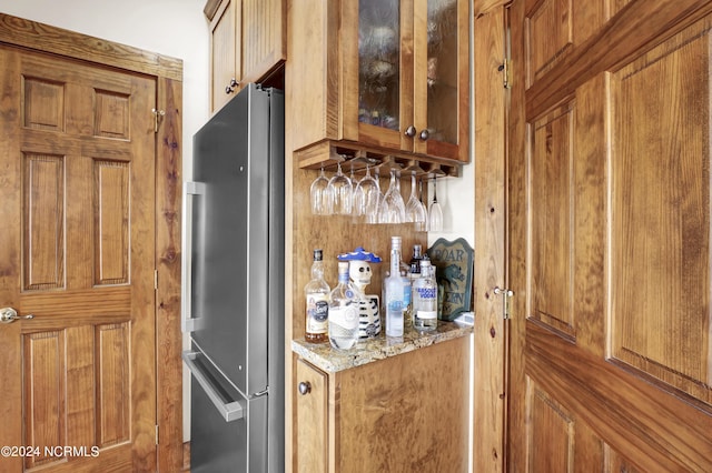 kitchen with brown cabinetry, light stone counters, glass insert cabinets, and freestanding refrigerator