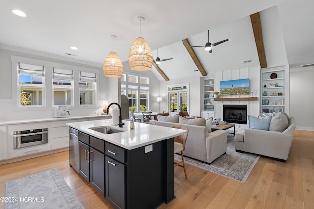 kitchen featuring stainless steel appliances, sink, decorative light fixtures, an island with sink, and vaulted ceiling with beams