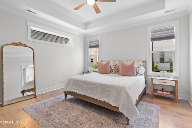 bedroom with hardwood / wood-style floors, ceiling fan, crown molding, and a tray ceiling