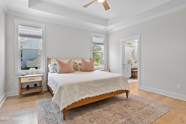 bedroom with light hardwood / wood-style floors, ceiling fan, a tray ceiling, and connected bathroom