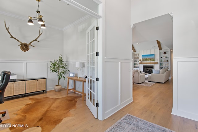 hall with an inviting chandelier, ornamental molding, and light hardwood / wood-style flooring