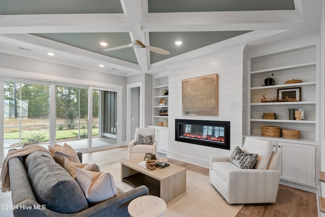 living room with light hardwood / wood-style flooring, beamed ceiling, ceiling fan, a large fireplace, and built in features