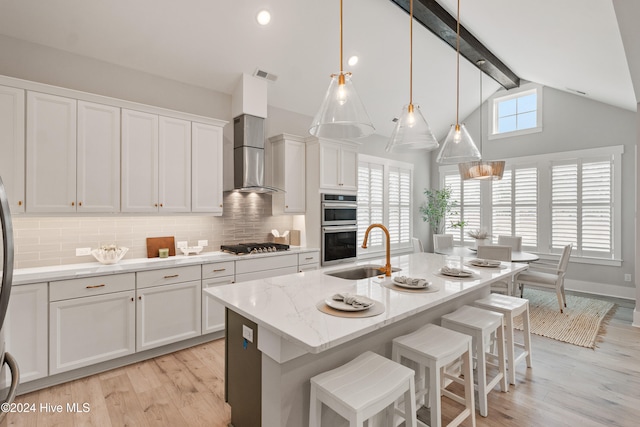 kitchen with sink, a kitchen island with sink, beam ceiling, white cabinetry, and light wood-type flooring