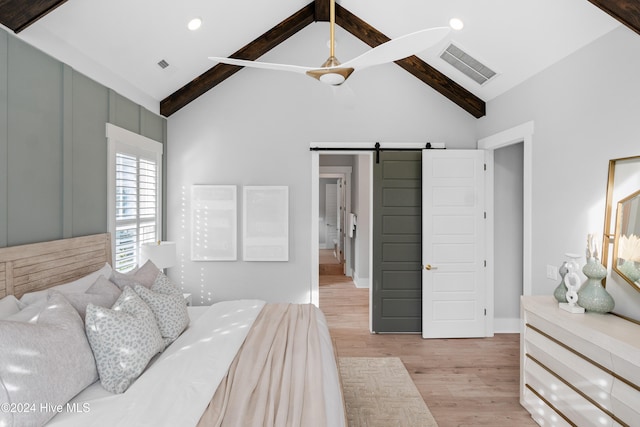 bedroom featuring light hardwood / wood-style floors, a barn door, high vaulted ceiling, ceiling fan, and beam ceiling