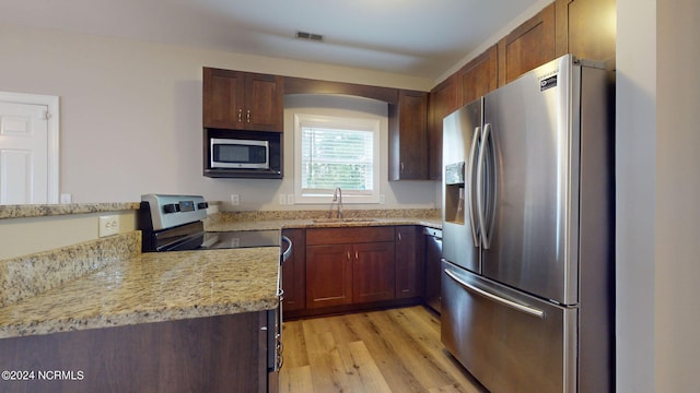 kitchen featuring light stone counters, sink, appliances with stainless steel finishes, and light hardwood / wood-style floors