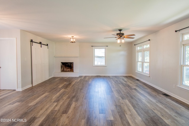 unfurnished living room featuring plenty of natural light, ceiling fan, a barn door, and wood-type flooring