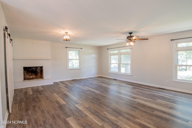 unfurnished living room featuring dark wood-type flooring, ceiling fan, a wealth of natural light, and a brick fireplace