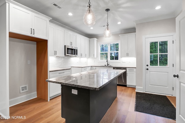 kitchen with a center island, white cabinetry, stainless steel appliances, and decorative light fixtures