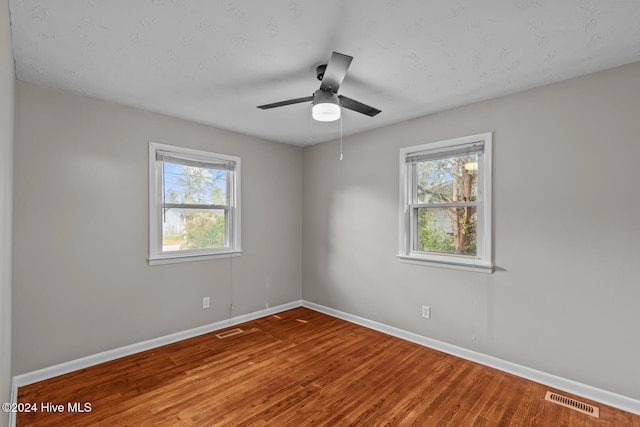 empty room with a wealth of natural light, ceiling fan, and hardwood / wood-style flooring