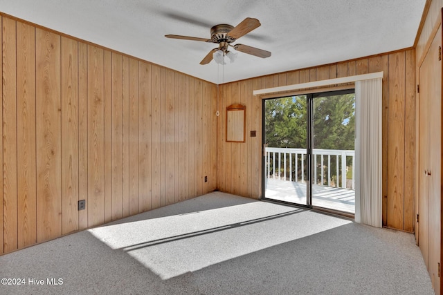 unfurnished room featuring wood walls, carpet floors, a textured ceiling, and ceiling fan