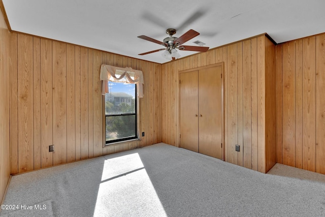 unfurnished bedroom with carpet flooring, wooden walls, and ceiling fan