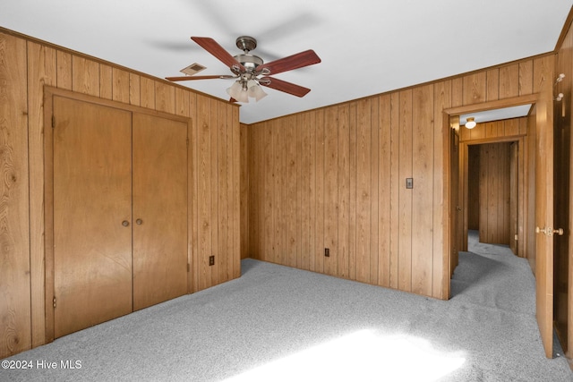 unfurnished bedroom with ceiling fan, light carpet, wooden walls, and a closet